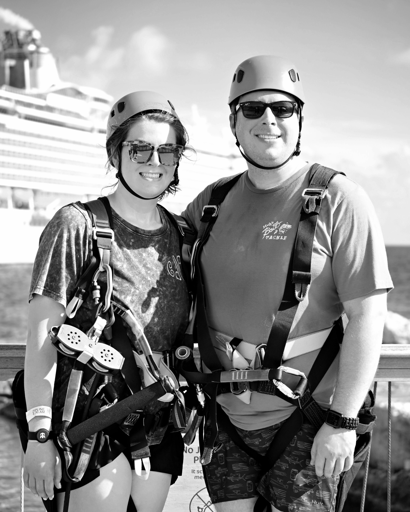 Isaiah and his partner wearing helmets and zip-line harnesses with a cruise ship behind them